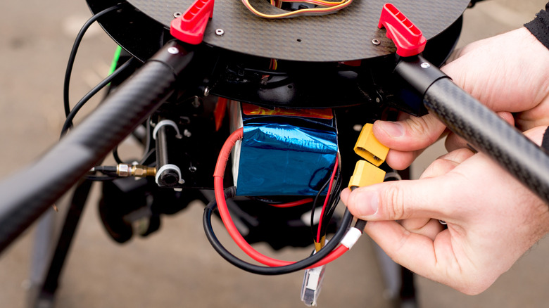 A pilot's hands sliding a high-capacity flight battery into the back of a drone.