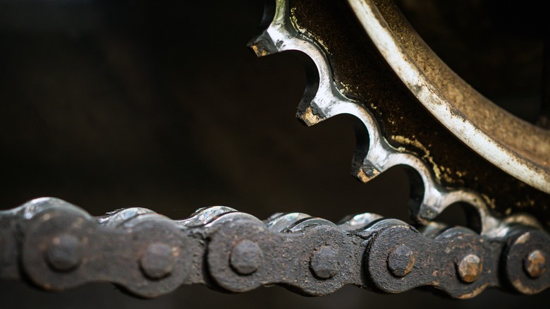 A dirty and grimy motorcycle chain resting on a worn sprocket.