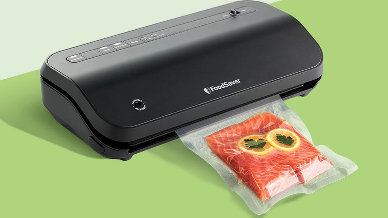 A FoodSaver machine vacuum-sealing a fresh salmon fillet in a plastic bag.