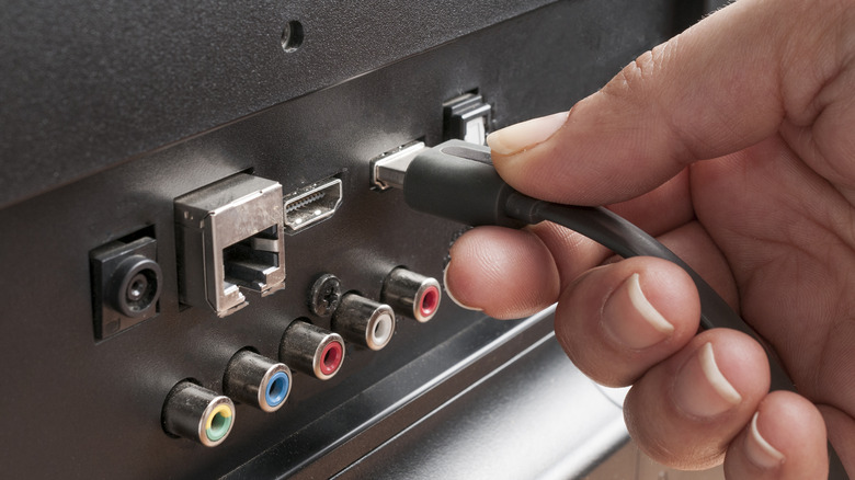 Close-up of a person attempting to plug an HDMI cable into the rear ports of a television.