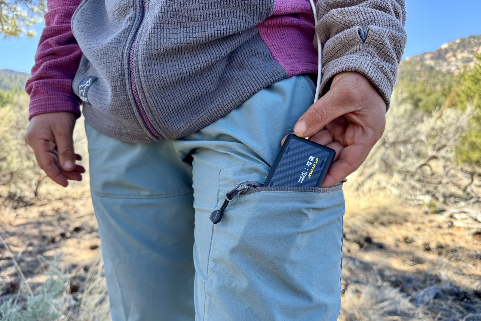 A small power bank being slid into the front pocket of a pair of jeans.