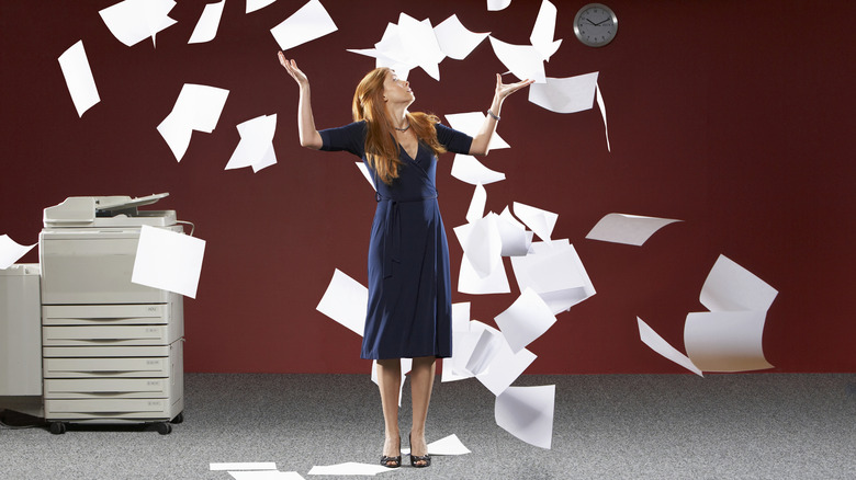 A woman tossing papers into the air next to an office photocopier.