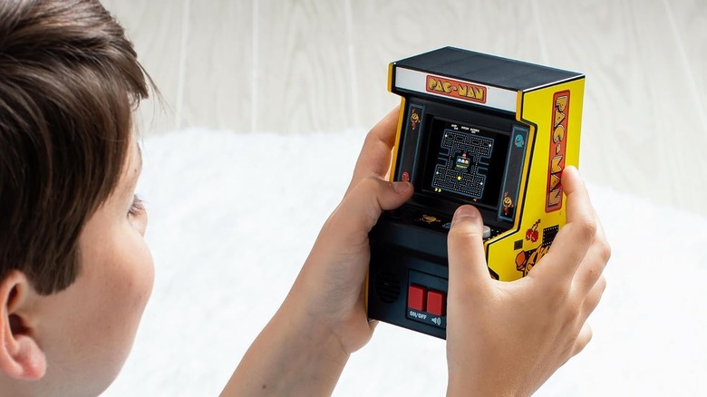 A child playing with a miniature retro Pac-Man arcade cabinet.