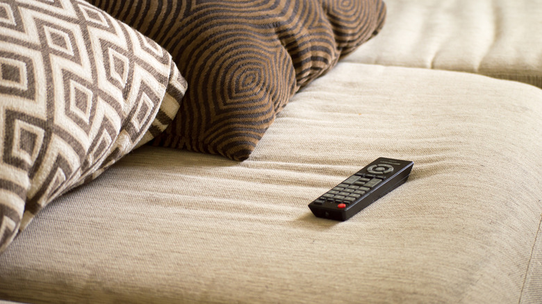 A black television remote sitting on a grey couch between cushions.