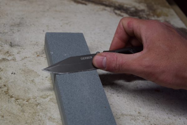 The 7cr17 steel blade of the Gerber Paraframe being sharpened against a professional whetstone.