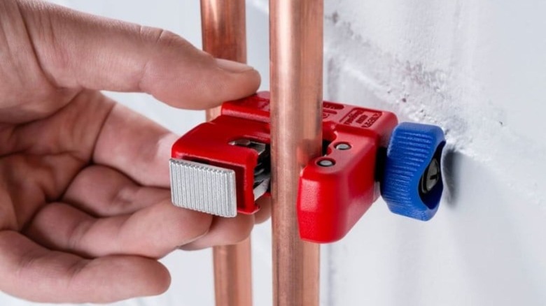 A Knipex TubiX S Pipe Cutter being used to cut a copper pipe in a tight space.