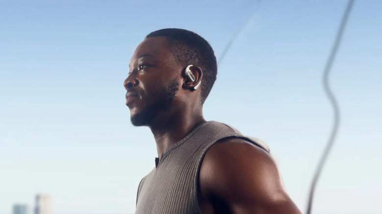 A man in activewear jogging outdoors while wearing white open-ear clip-on earbuds.