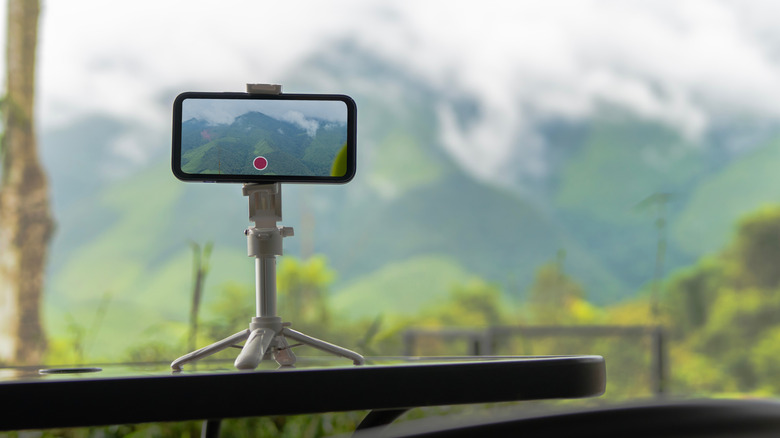 A smartphone mounted on a small tripod against a mountain landscape.
