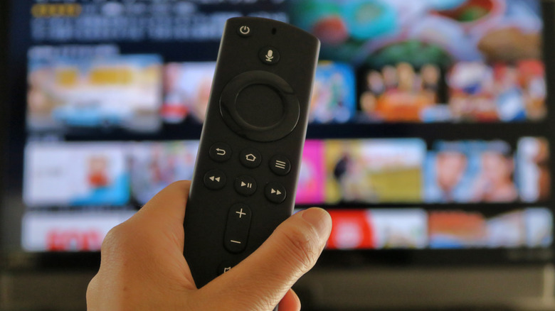 Close-up of an Amazon Fire TV Stick remote control with a television in the background.