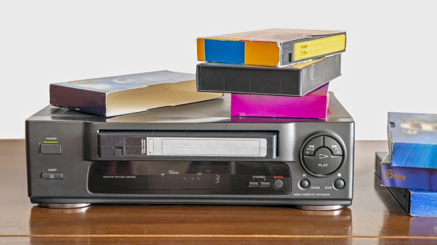 A shelf stacked with several VHS tapes in their protective cardboard and plastic sleeves.