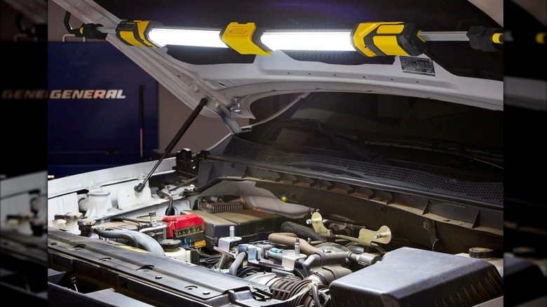Braun underhood light securely clamped to the edges of an open car hood.