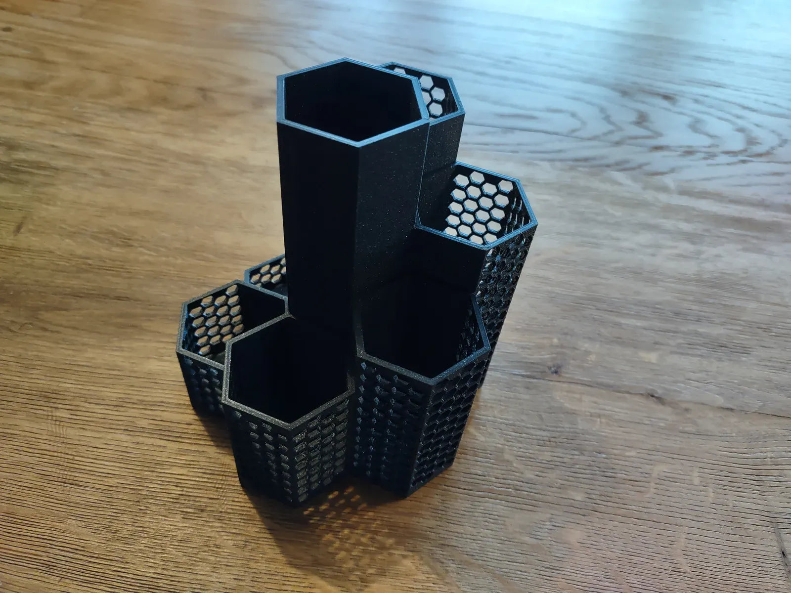 A black hexagonal modular desk organizer holding various office supplies on a wooden surface.