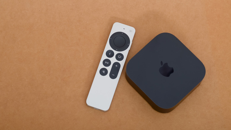 An Apple TV 4K unit and the silver Siri Remote placed on a wooden surface.