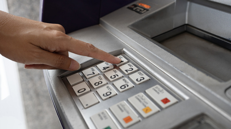 A person's hand pressing a number on a metal ATM keypad.