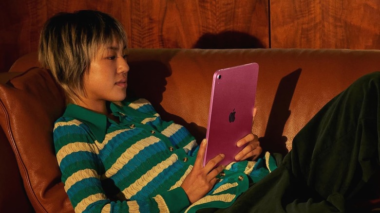 A person in a striped sweater reclining on a couch while using an iPad.