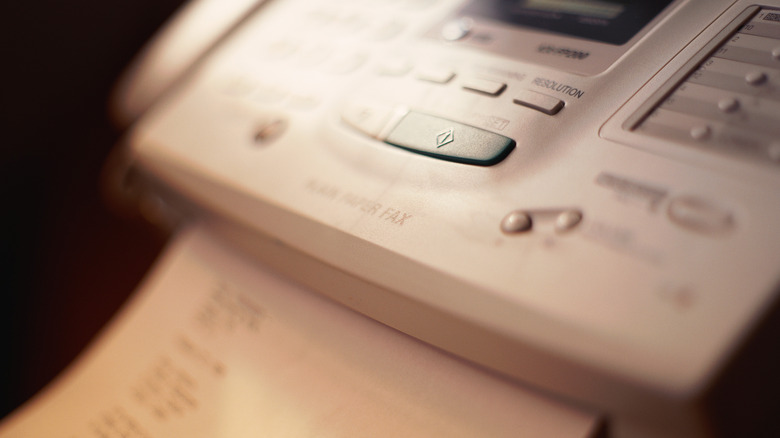 Close-up of a vintage 1980s fax machine with control buttons and paper feed.
