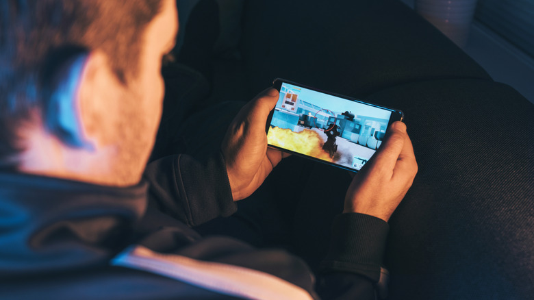 A person sitting and playing an action-shooter mobile game on their smartphone.