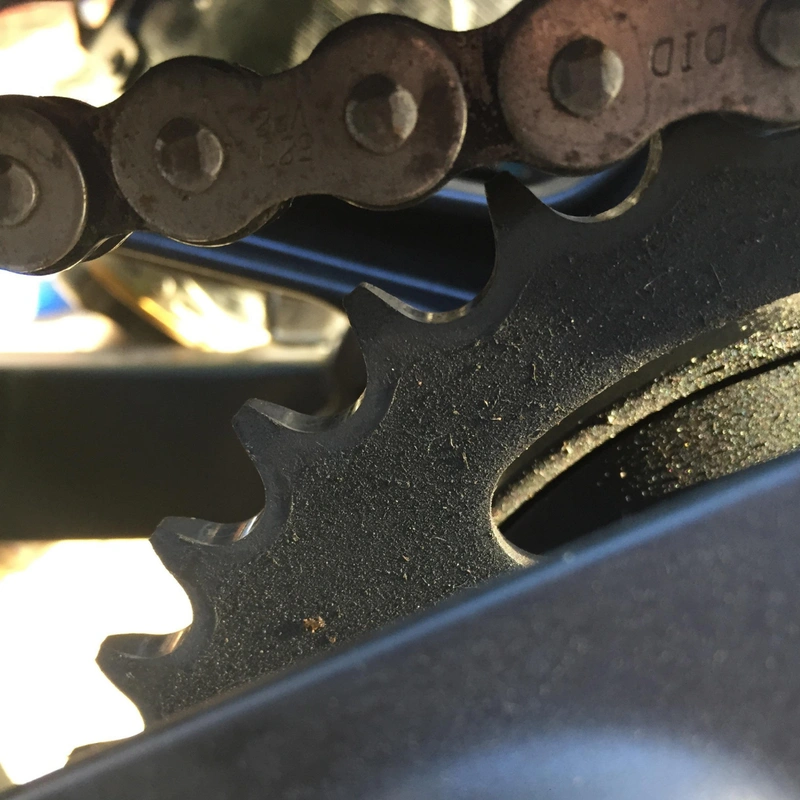A used motorcycle sprocket that still has squared-off tooth tips despite being dirty.