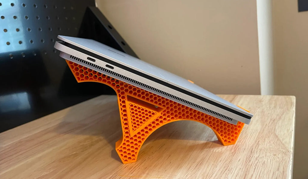 A black 3D printed laptop stand featuring a lightweight but sturdy honeycomb lattice pattern.
