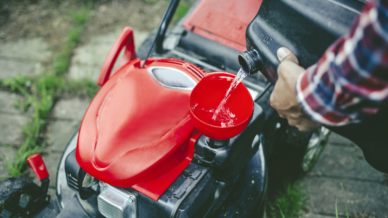 A person preparing a gasoline-powered lawn mower for yard work.