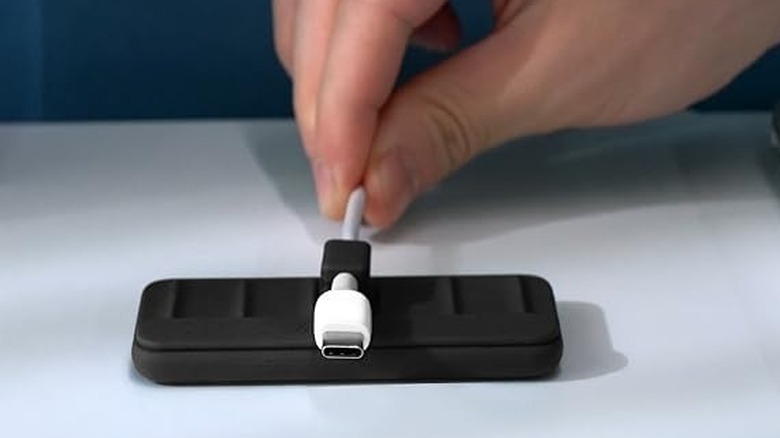 A hand bringing a USB-C cable clip toward the magnetic base of the Anker organizer.