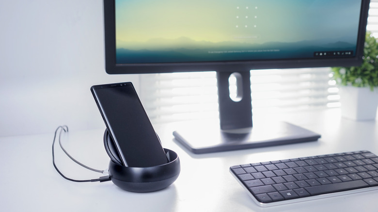 A Samsung Galaxy smartphone connected to a desktop monitor displaying the Samsung DeX interface.