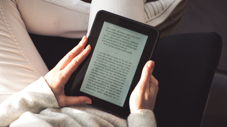 A person sitting comfortably on a sofa holding a thin electronic reader.