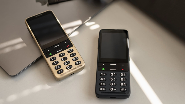 Two BlindShell Classic 3 phones in black and gold showing large physical buttons and high-contrast screens.