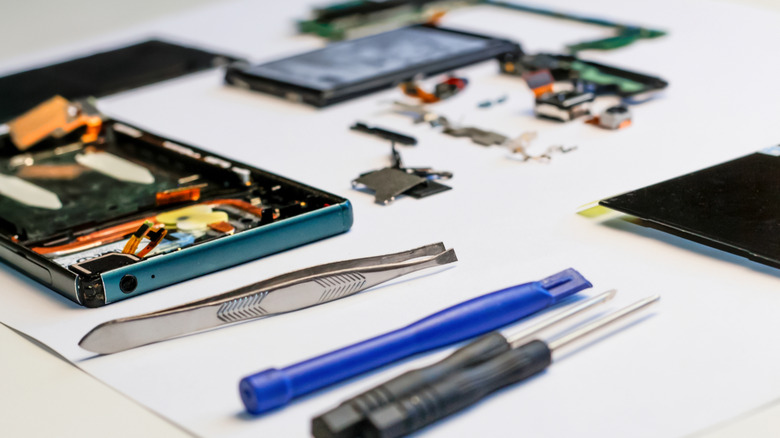 A smartphone undergoing repair next to precision tools.
