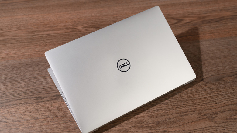 The back of a Dell laptop showing the circular logo resting on a wooden surface.
