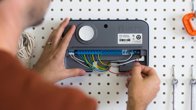 Hands installing a white Rachio 3 Smart Sprinkler Controller onto a wall.
