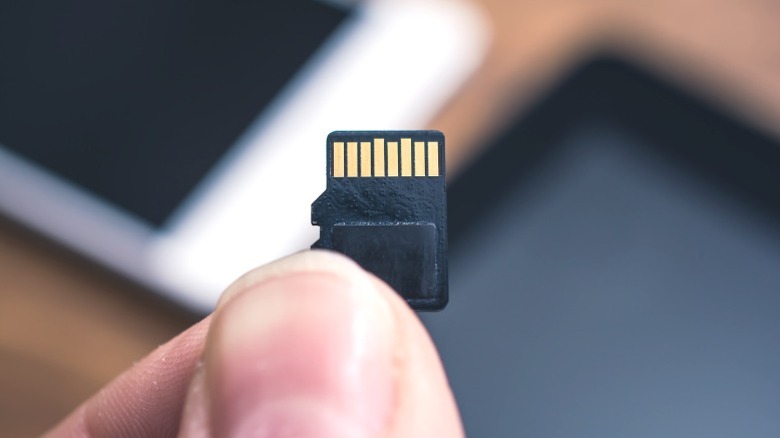 A man holding a small microSD card next to a modern smartphone.