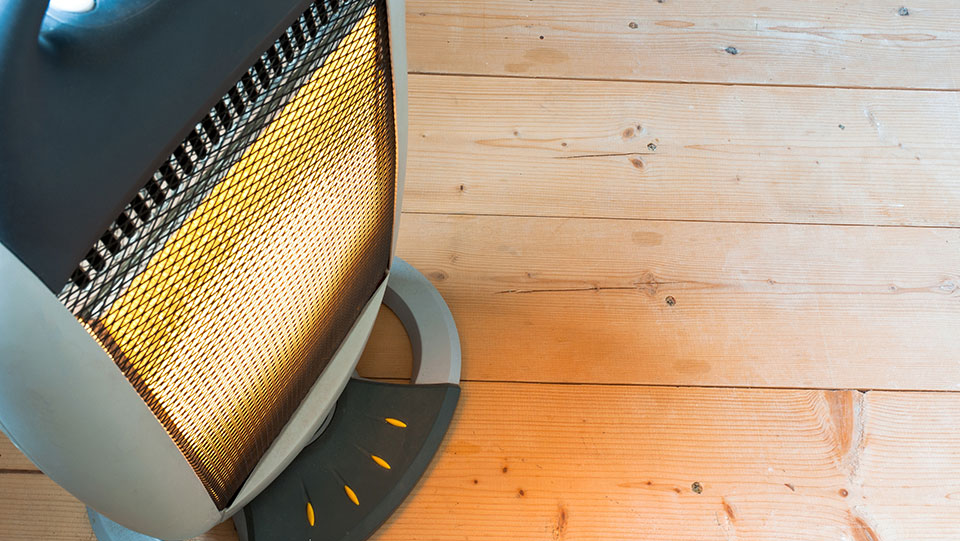 A portable white electric space heater placed on a wooden floor.