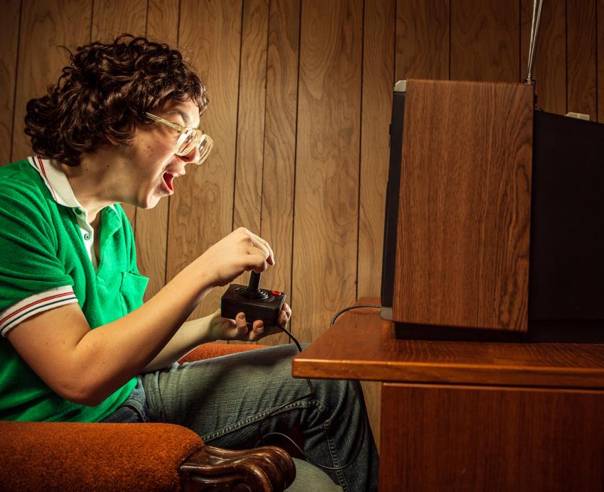 A young person sitting in front of a TV screen playing an early 8-bit home video game console.