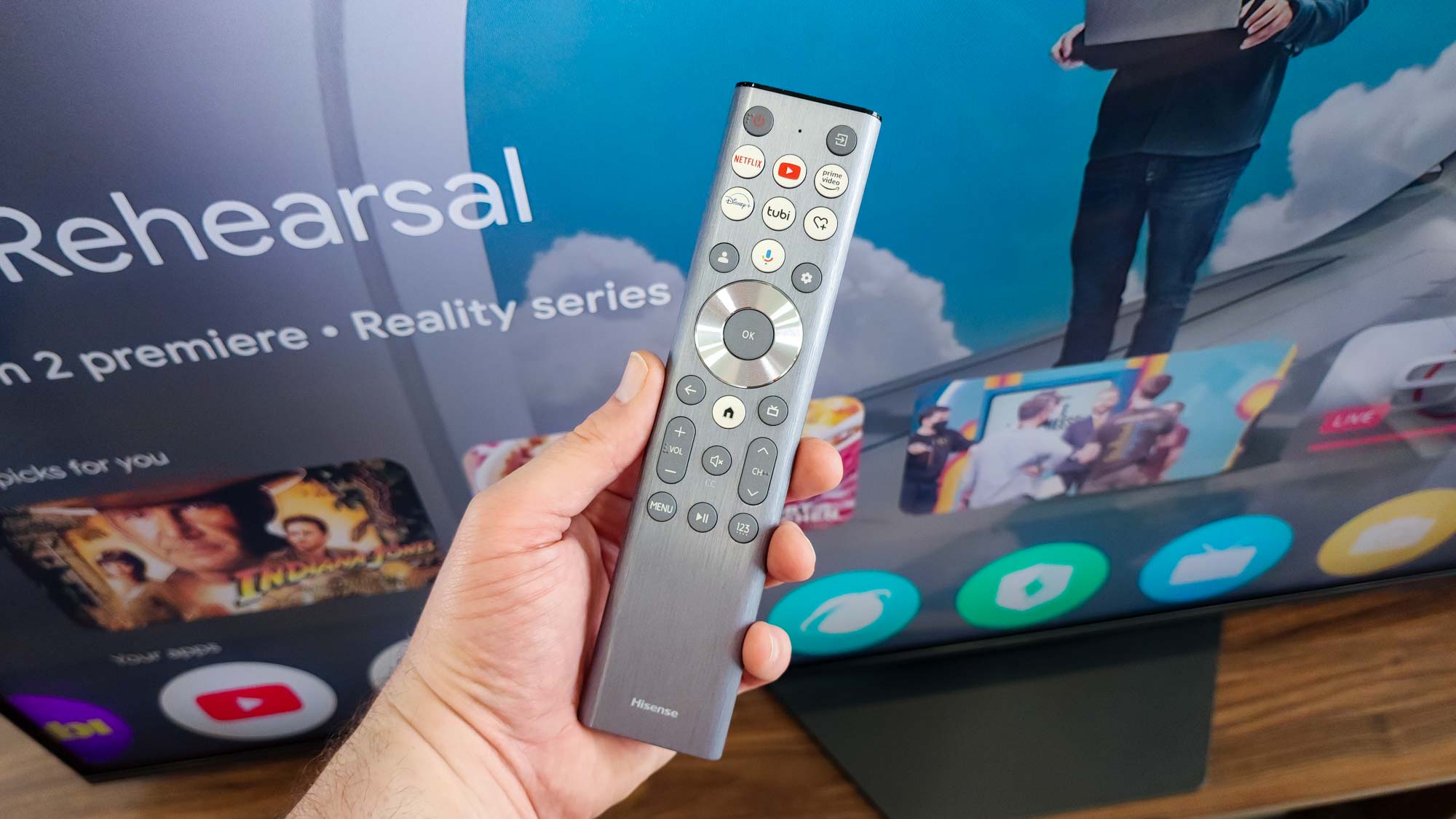 A hand-held Hisense TV remote control pointing toward a screen.