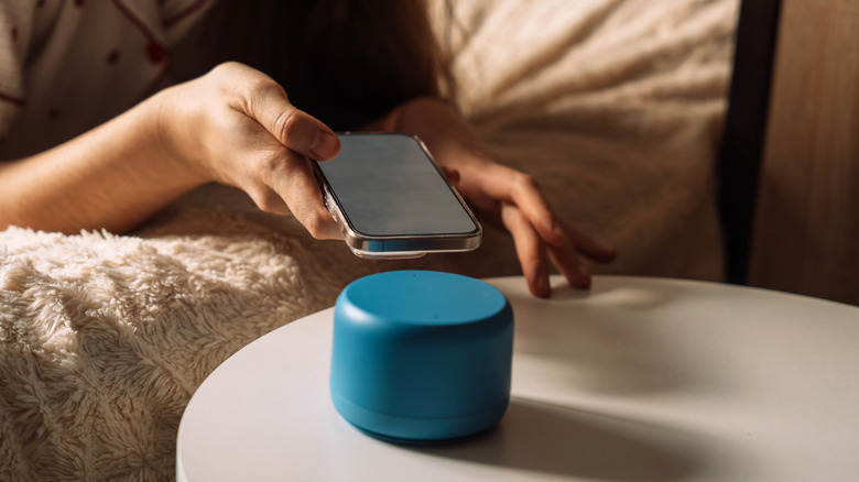A close-up of a person using a smartphone to configure a small smart speaker.