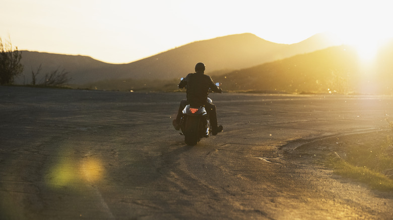A motorcyclist riding on a coastal road during sunset.