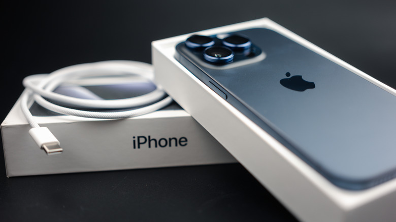 An iPhone 15 next to its retail box and a braided USB-C charging cable.