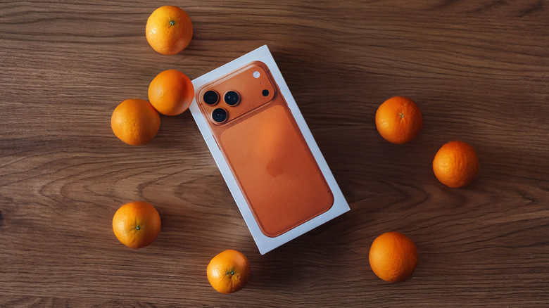 An iPhone 17 Pro Max in its retail box with a decorative orange background.