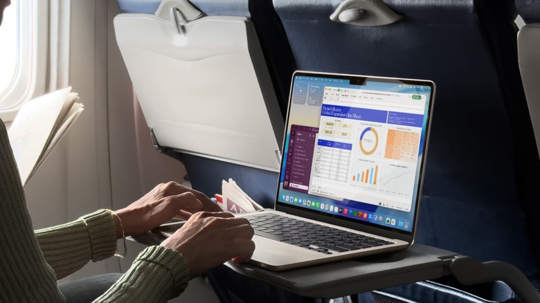 A traveler using a MacBook Air on an airplane tray table.
