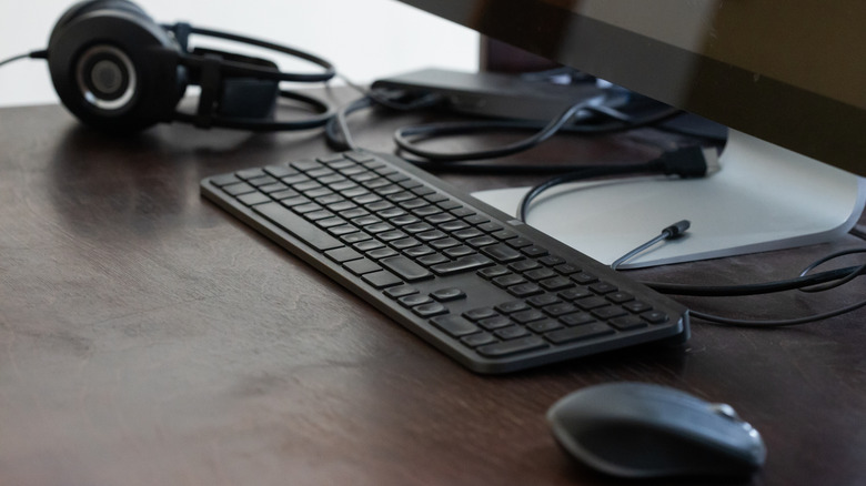 A keyboard and mouse setup in front of a monitor on a clean wooden desk.