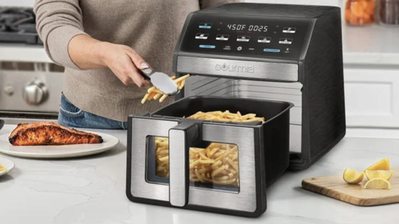 A woman using a Gourmia digital air fryer to prepare a batch of crispy french fries.