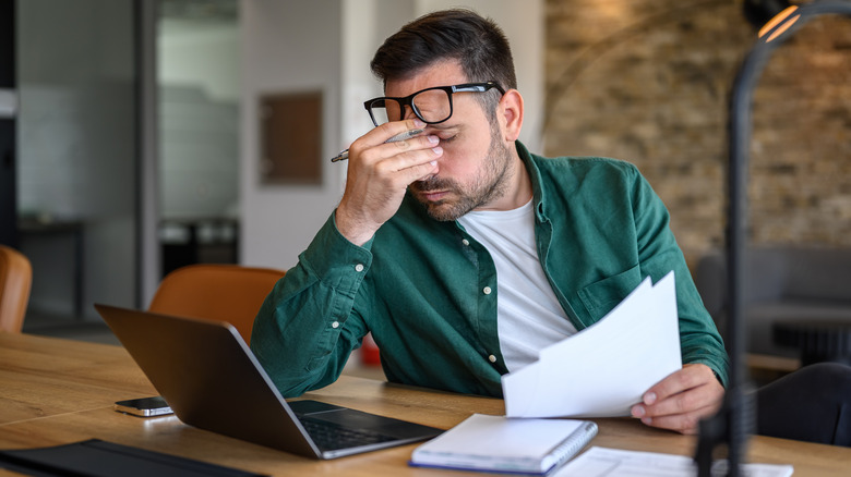 A person rubbing their eyes while using a laptop, suggesting fatigue or a headache.