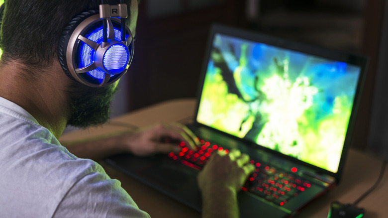 A gamer using a backlit gaming laptop in a dark room.