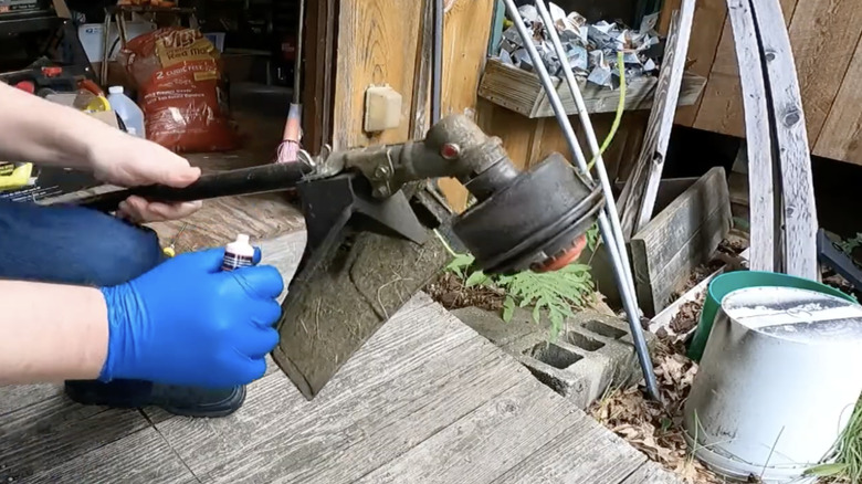 Hands in blue protective gloves applying grease to the gear head housing of a weed eater.