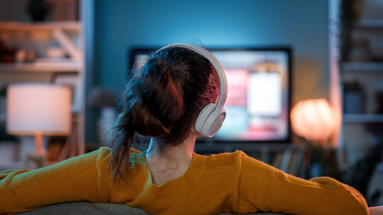 A woman wearing large headphones while watching a television screen in a living room.