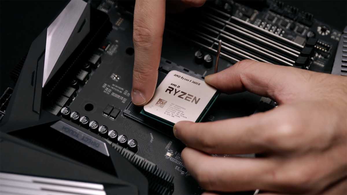 A technician's hand carefully lowering an AMD Ryzen processor into a motherboard's AM5 socket.