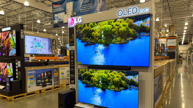 A variety of high-end OLED TVs displayed on shelves in a retail electronics store.