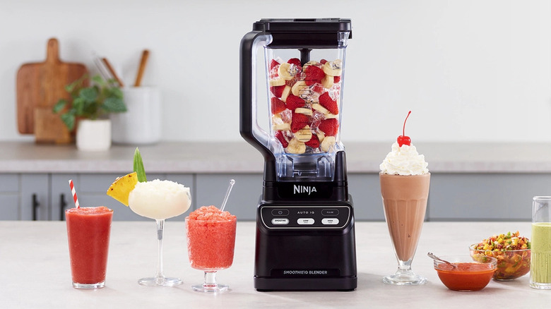 A Ninja professional blender on a kitchen counter surrounded by fresh fruit and finished smoothies.
