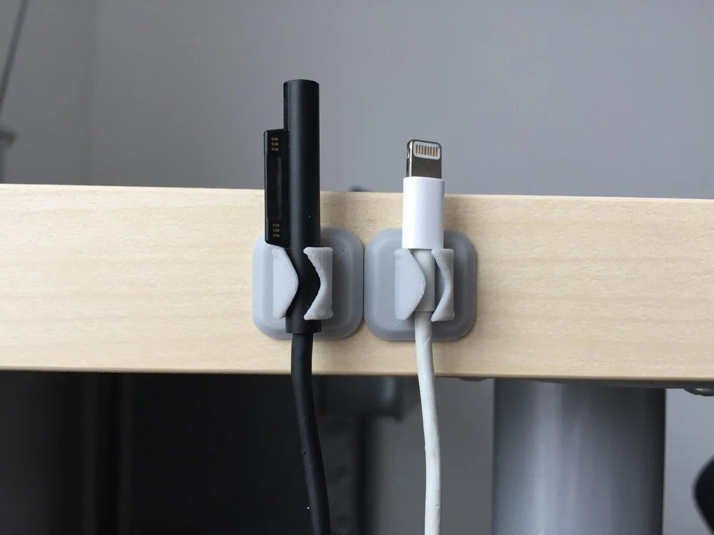 A small 3D printed plastic clip holding multiple colored cables neatly against a desk edge.